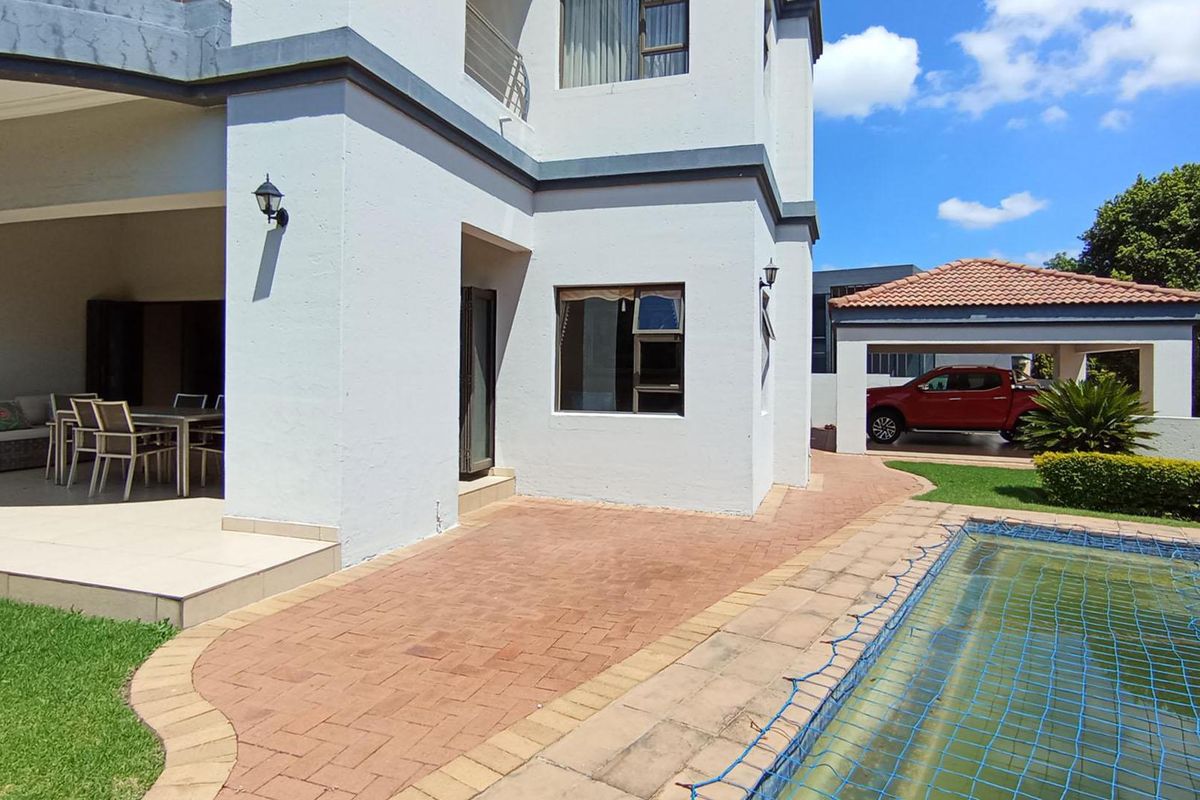 Rear exterior view featuring a covered patio, paved walkway, swimming pool with safety net, and a detached carport.