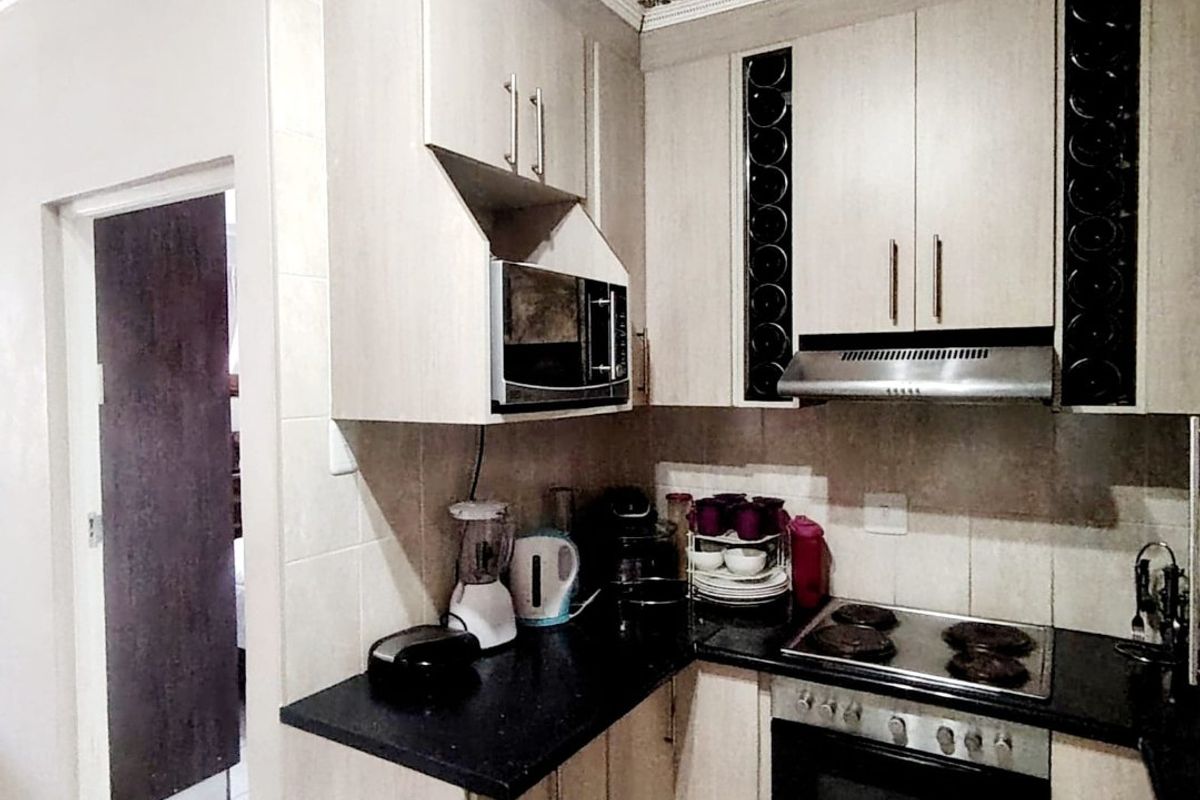 Compact kitchen featuring light-toned cabinetry, black countertops, integrated oven and hob, and decorative ceiling cornicing.