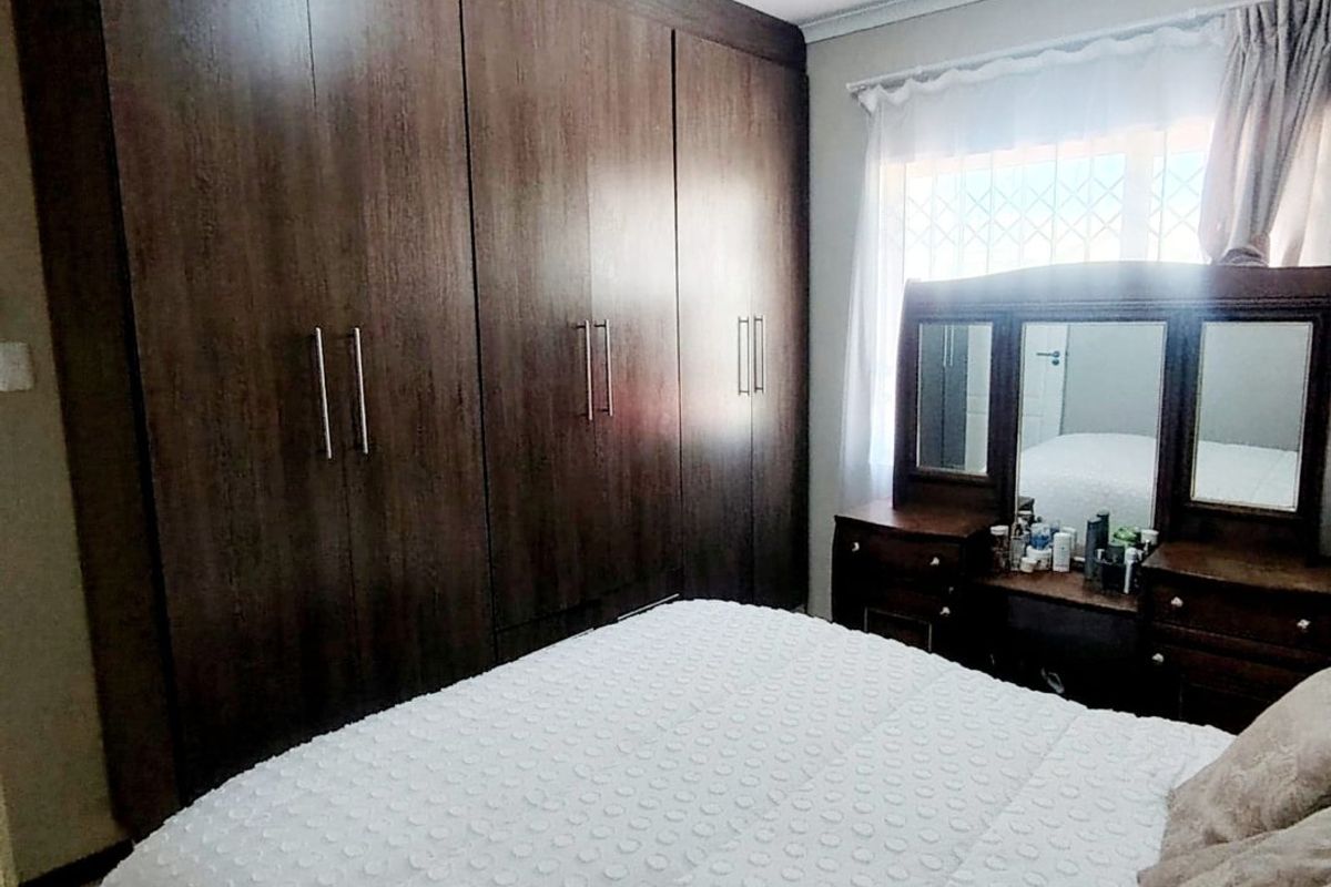 A bedroom featuring dark wood built-in cupboards and a window with security bars, providing functional storage and natural light.