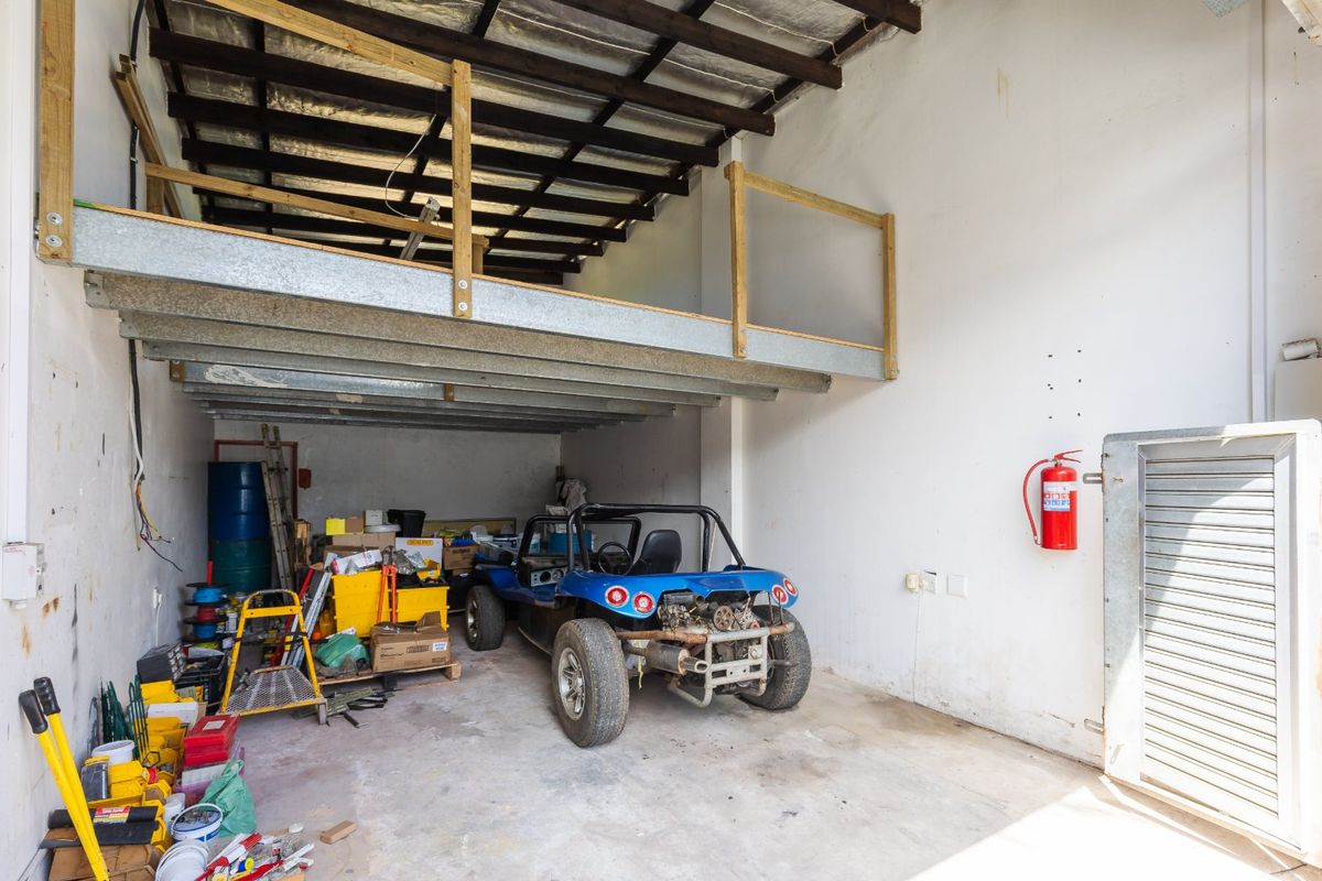 Industrial garage space featuring a mezzanine level, exposed timber rafters, and a roller shutter door, suitable for storage or workshop use.