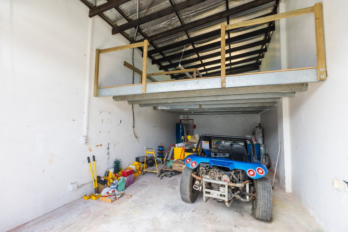 Industrial garage space featuring a mezzanine level, exposed steel roof structure, and concrete flooring, suitable for storage or workshop use.