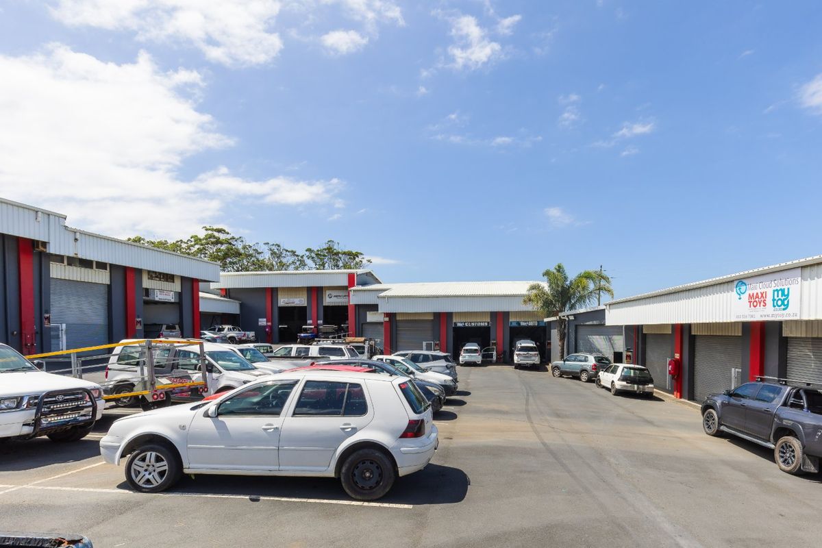 Industrial complex featuring multiple units with roller shutter doors, paved parking area, and metal cladding exterior.