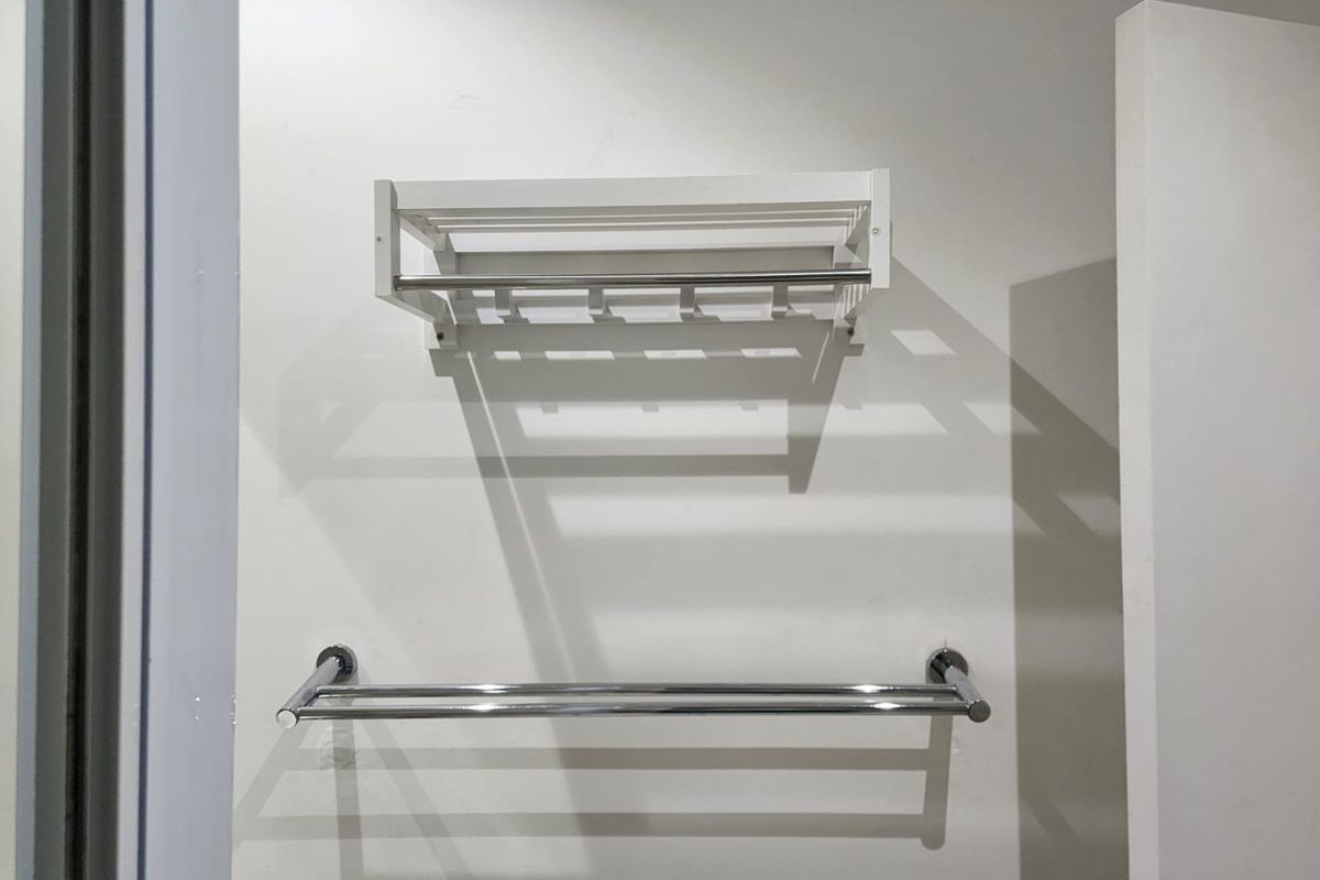 A clean bathroom wall featuring a white wall-mounted towel rack and a modern chrome double towel rail.