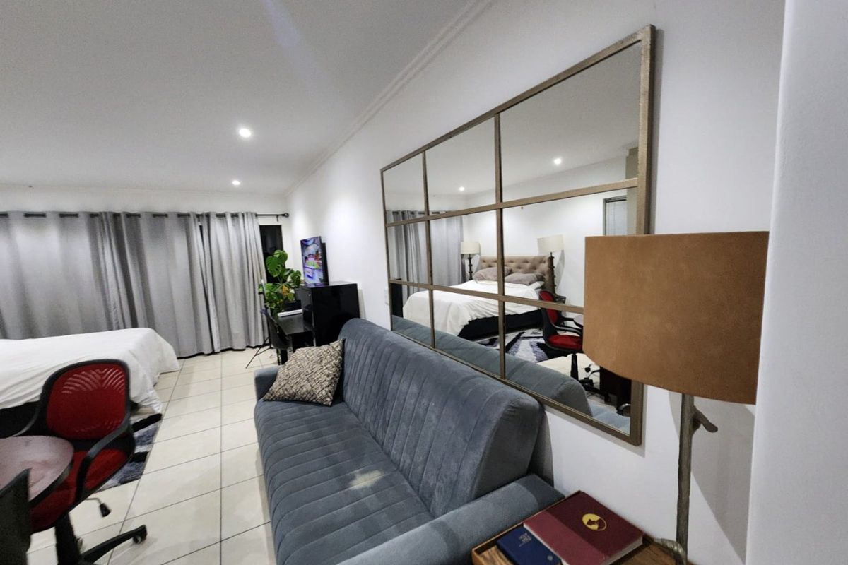 Spacious bedroom featuring tiled flooring, recessed lighting, and a large decorative wall mirror, offering a versatile layout for sleeping and living areas.