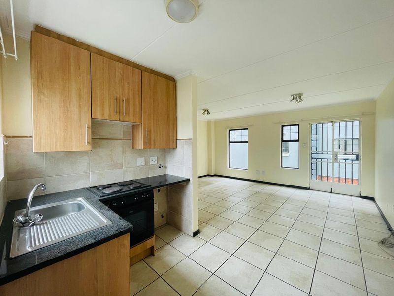 Open-plan kitchen and living area featuring tiled flooring, built-in wooden cabinetry, and direct access to a balcony through a security gate.