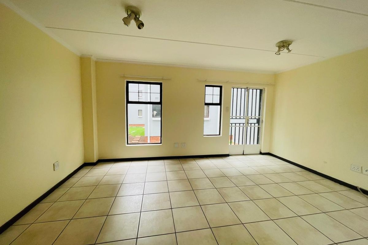 An empty, open-plan living area featuring neutral tiled flooring, security gate access, and ceiling-mounted spotlights, offering a blank canvas for personalization.