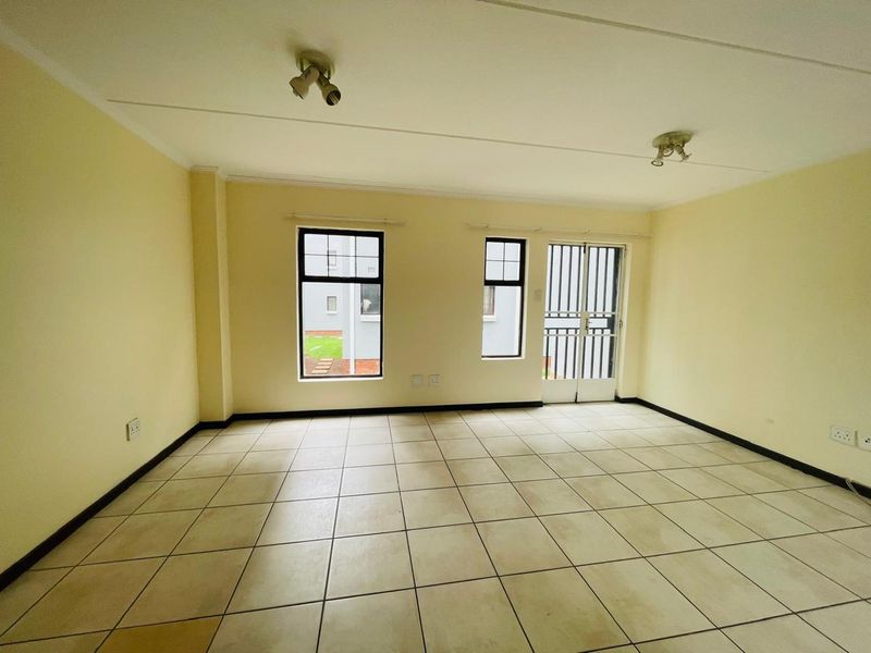 An empty, open-plan living area featuring neutral tiled flooring, security gate access, and ceiling-mounted spotlights, offering a blank canvas for personalization.