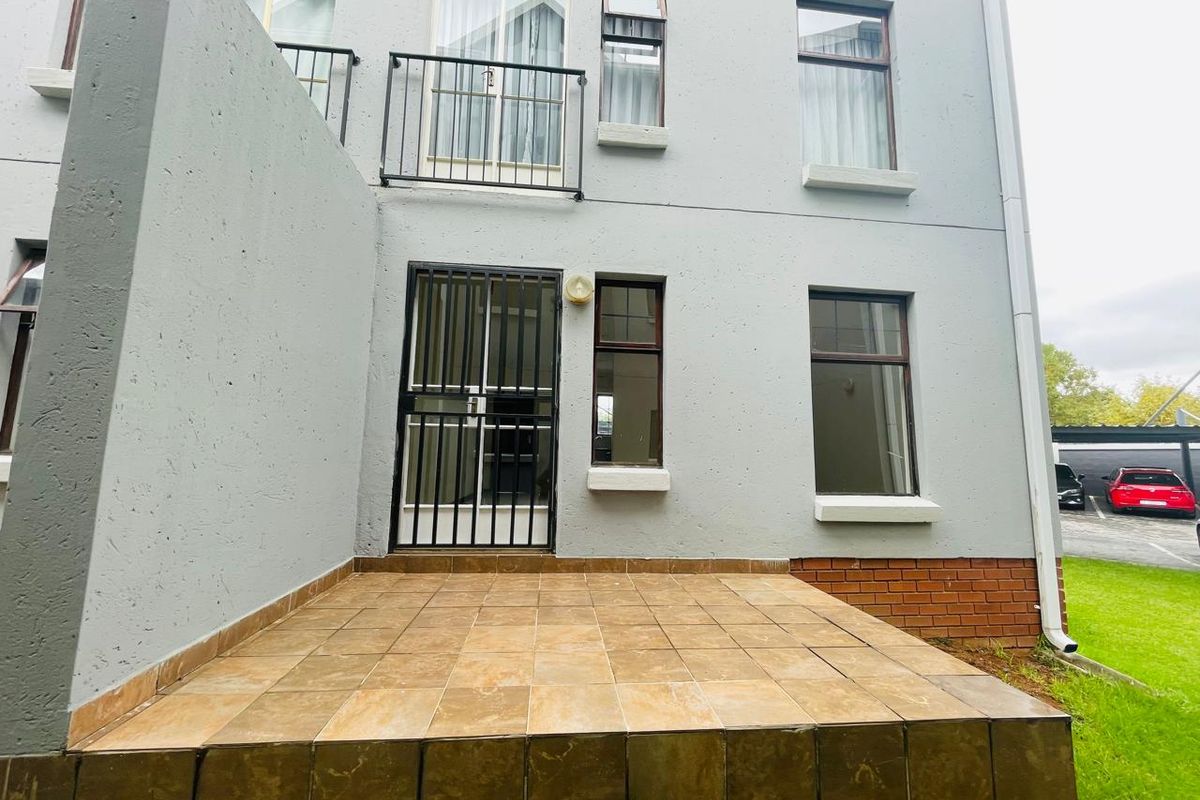 Rear exterior view of the apartment featuring a tiled patio, security gate, and upper-level balcony with metal railings.