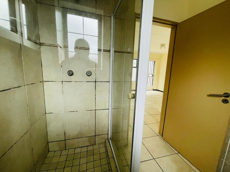 A dated bathroom featuring a shower enclosure with tiled walls and flooring, showing signs of wear and requiring cosmetic updates.