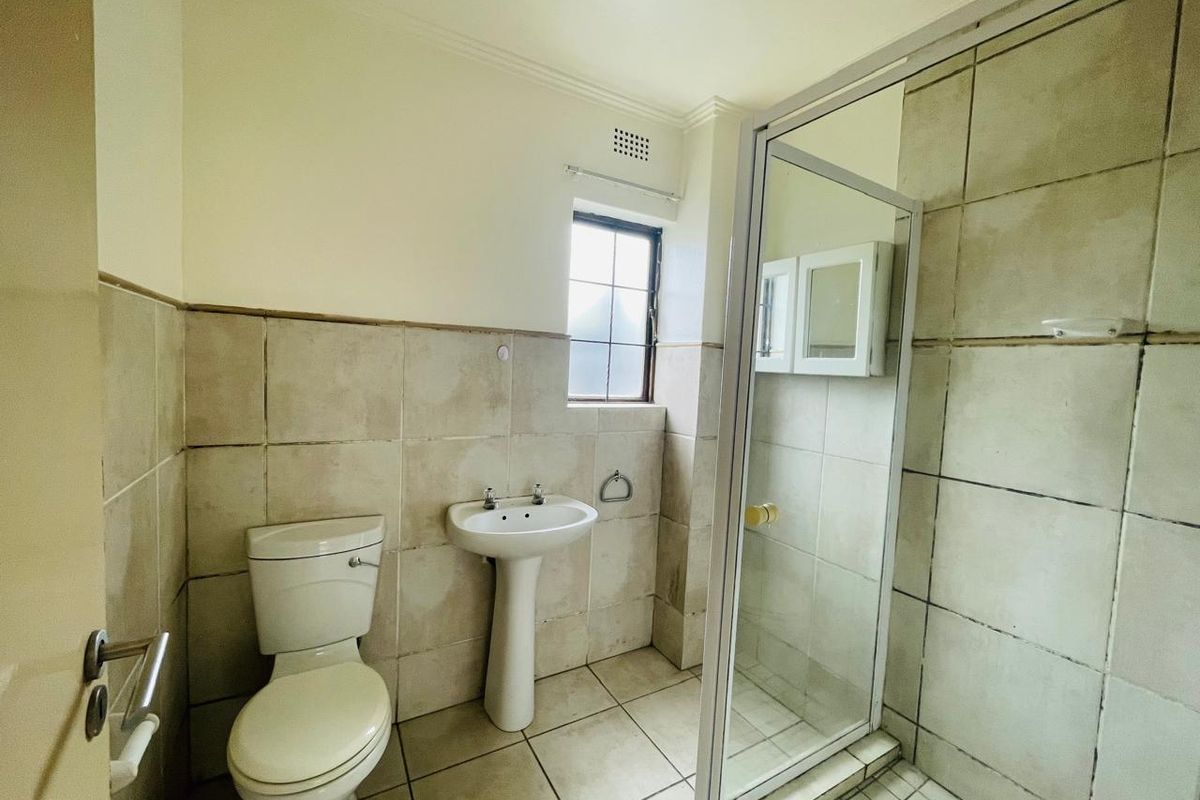 A functional bathroom featuring a pedestal sink, toilet, and a glass-enclosed shower with neutral wall and floor tiling.