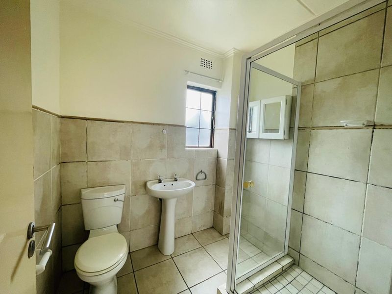 A functional bathroom featuring a pedestal sink, toilet, and a glass-enclosed shower with neutral wall and floor tiling.