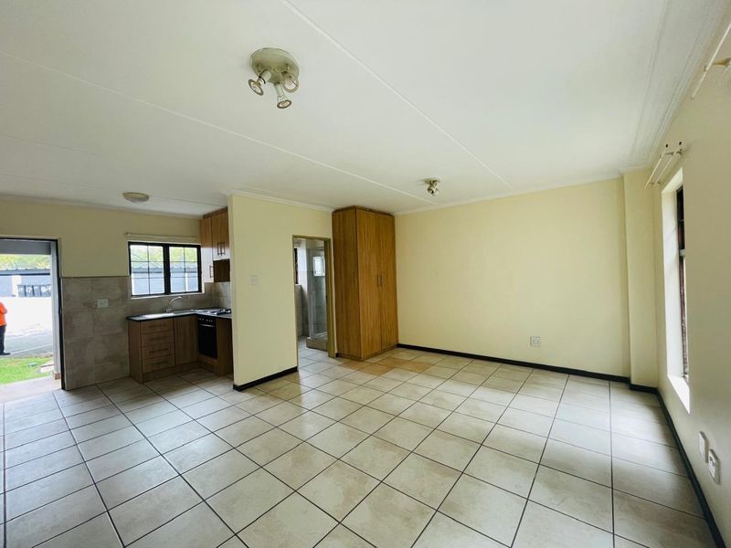 Open-plan living area featuring tiled flooring, a compact kitchen with built-in cabinetry and appliances, and a built-in storage cupboard.
