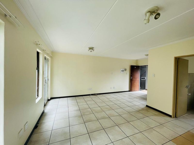 An empty, open-plan living area featuring tiled flooring, neutral wall finishes, and direct access to a secure entrance.