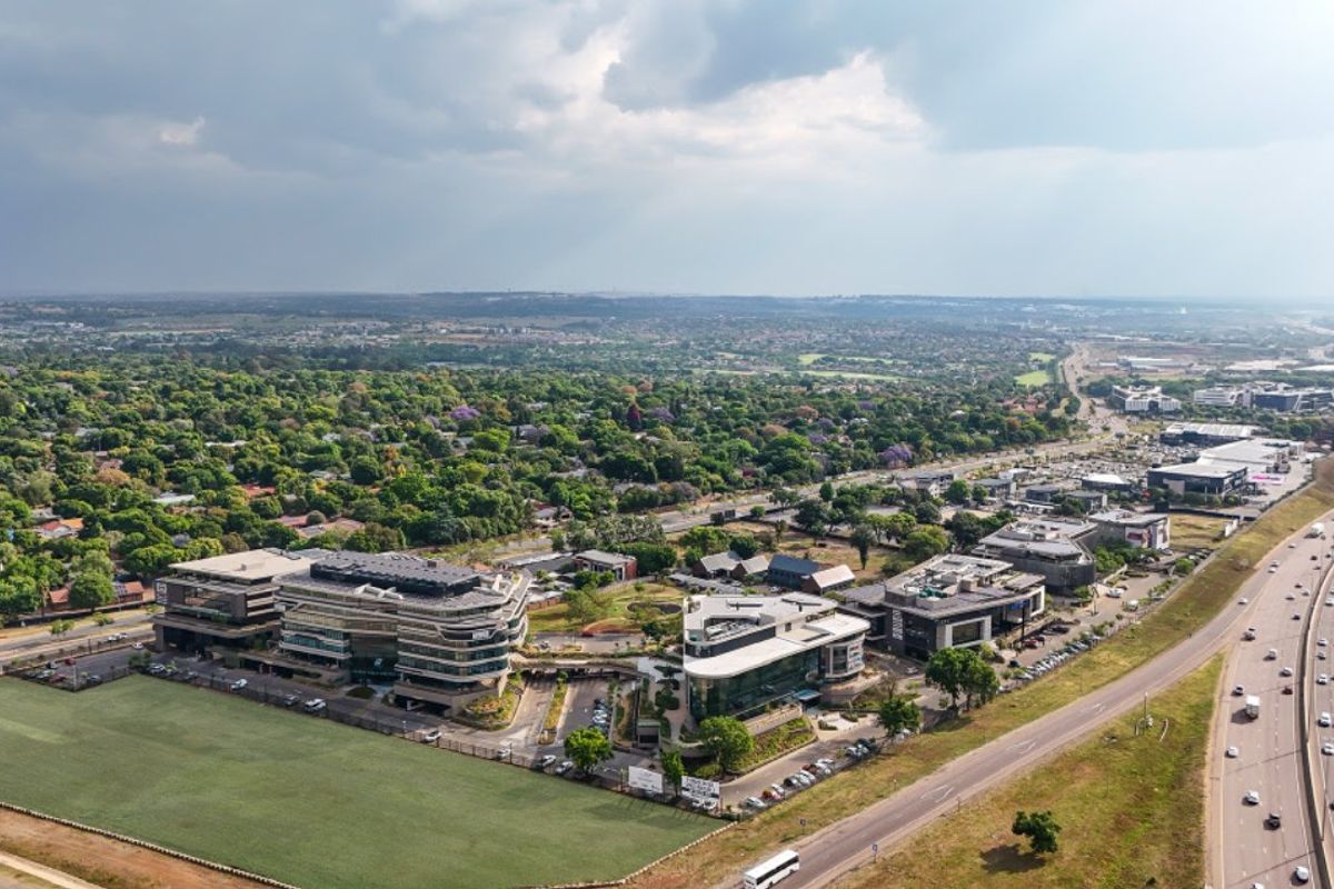 Aerial view of a modern commercial office park situated adjacent to a major highway, featuring landscaped grounds and extensive parking facilities.