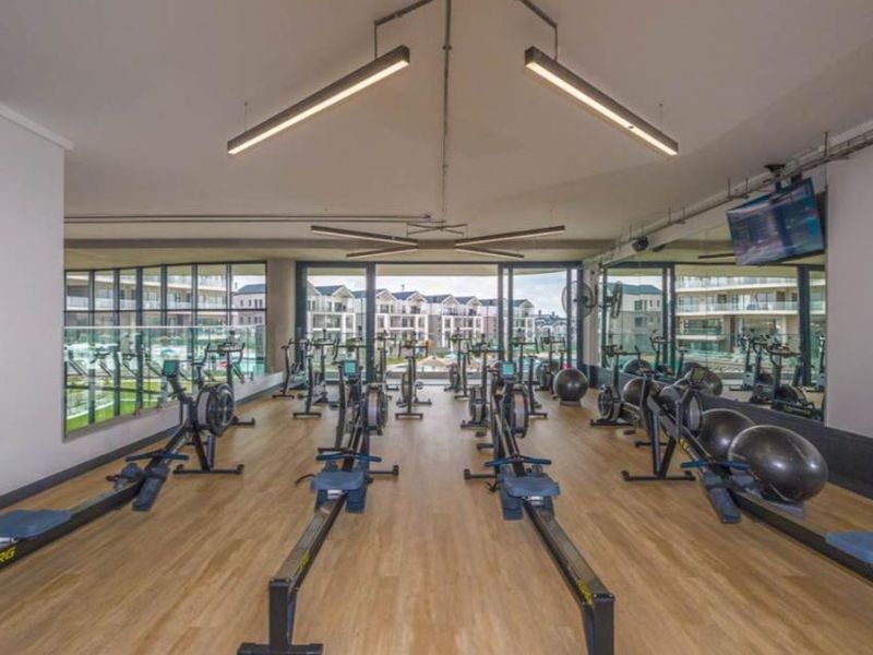 A modern, well-lit gym facility featuring timber-look flooring, large wall mirrors, and sliding glass doors leading to an outdoor area.