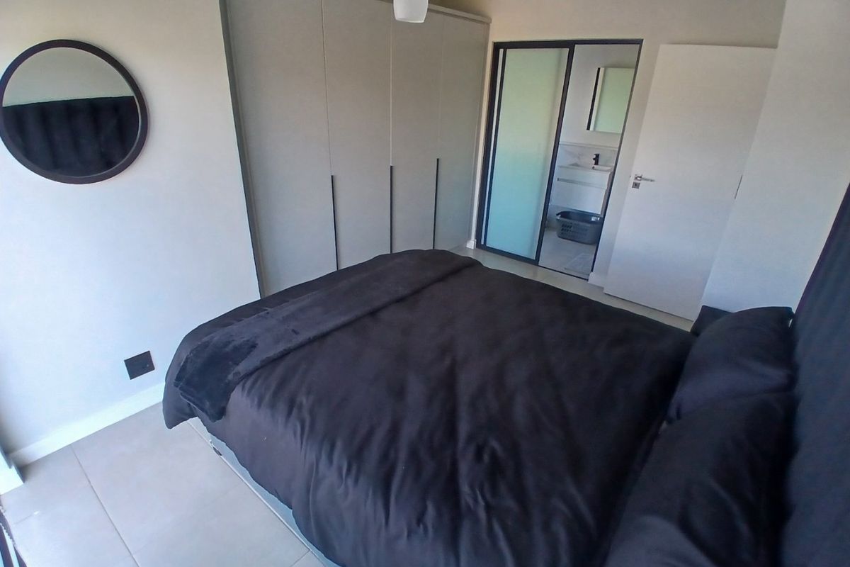 Modern bedroom featuring neutral walls, tiled flooring, and ample built-in cupboard space, with direct access to an en-suite bathroom.