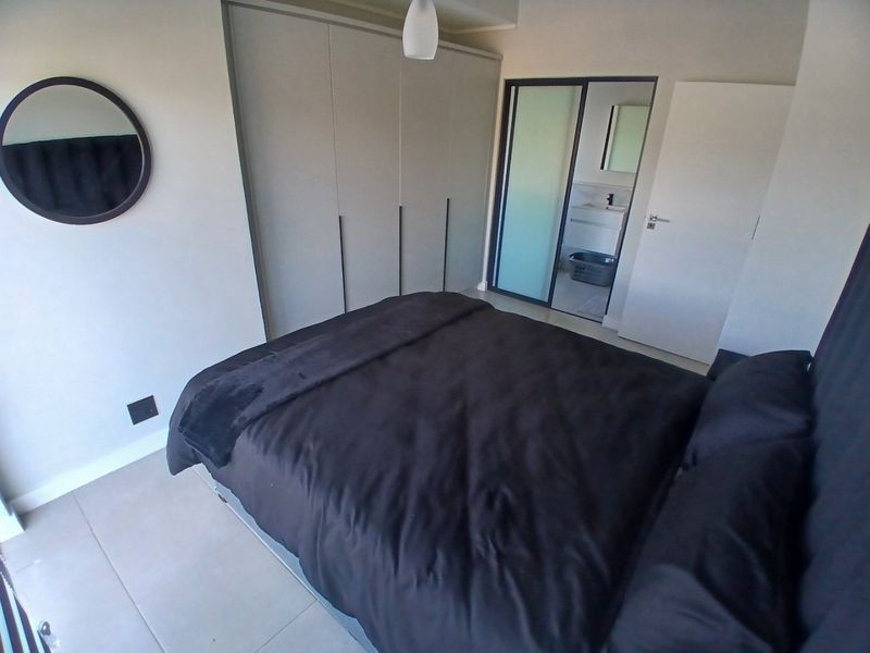 Modern bedroom featuring neutral walls, tiled flooring, and ample built-in cupboard space, with direct access to an en-suite bathroom.