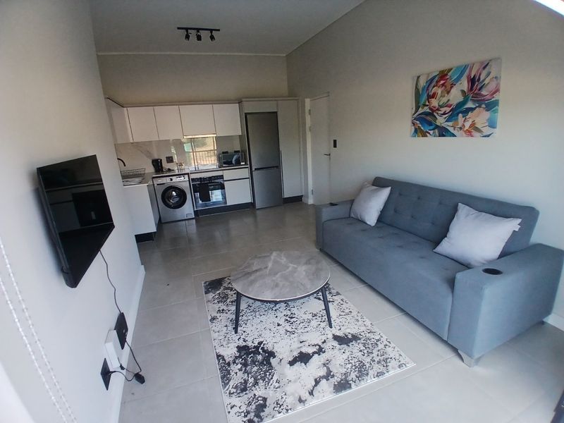 Modern open-plan living area featuring a compact kitchen with built-in cabinetry, integrated appliances, and sleek tiled flooring throughout.