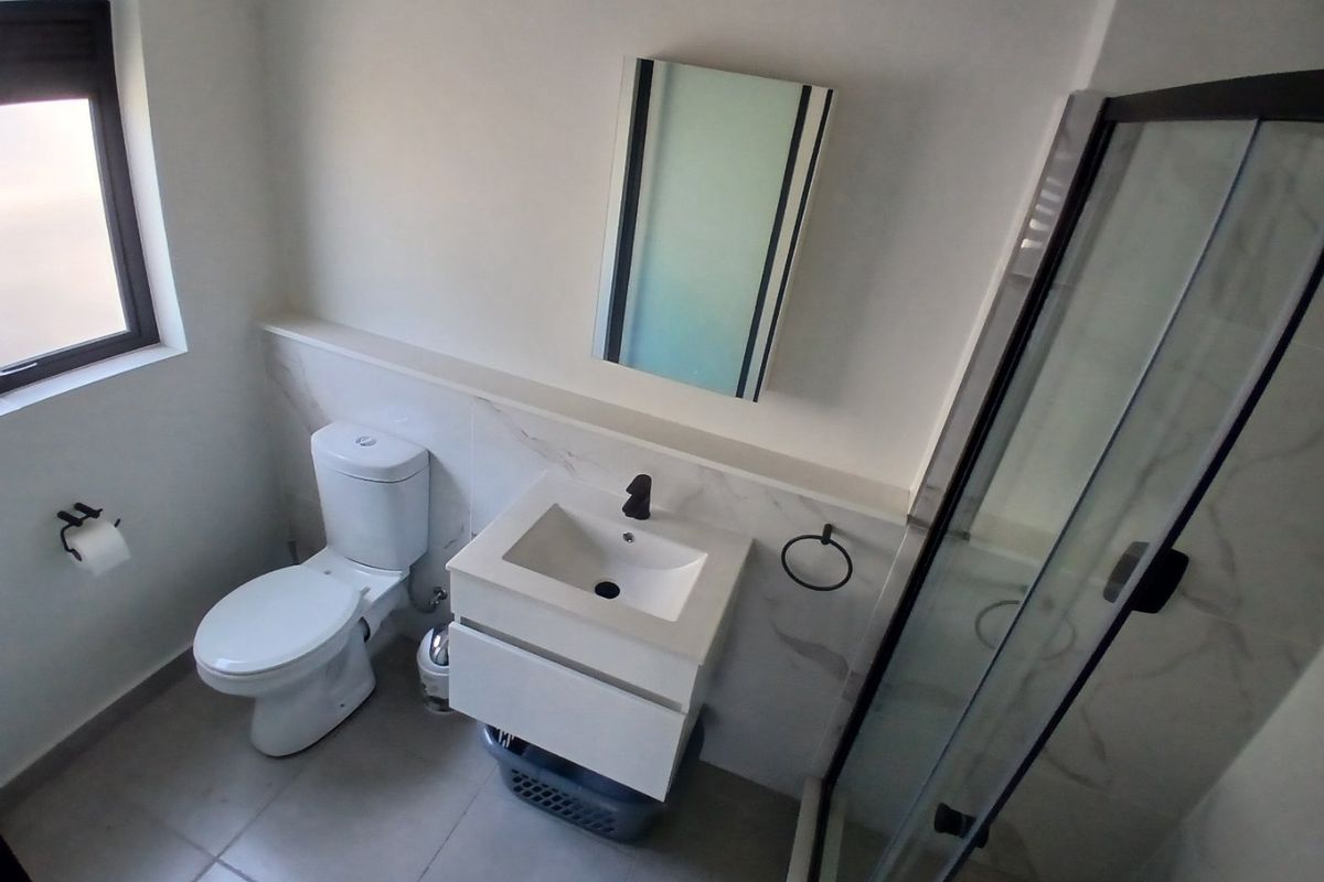 Modern bathroom featuring a wall-mounted vanity, glass shower enclosure, toilet, and contemporary black fixtures with neutral wall tiles.