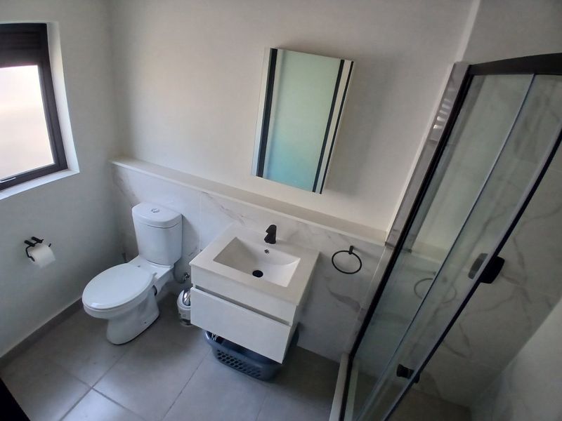 Modern bathroom featuring a wall-mounted vanity, glass shower enclosure, toilet, and contemporary black fixtures with neutral wall tiles.