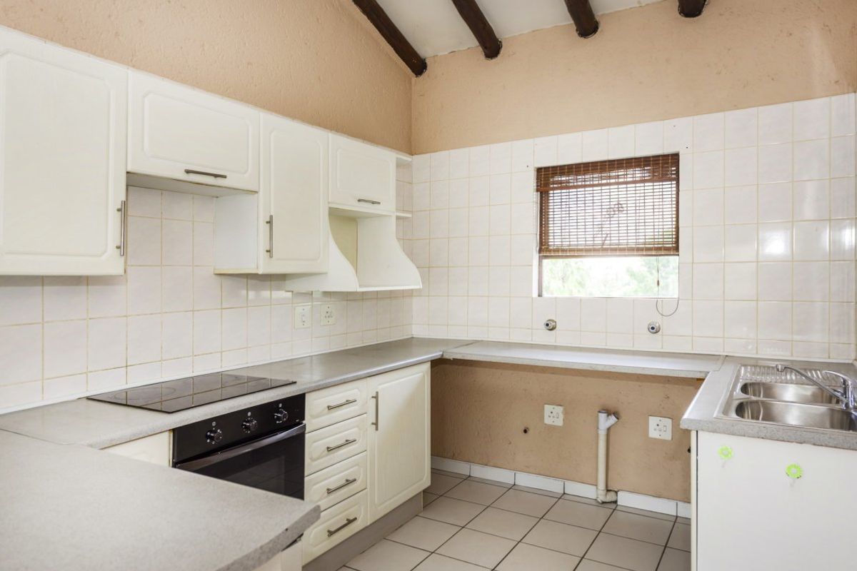 A functional kitchen featuring white cabinetry, built-in oven and hob, double sink, and exposed timber ceiling beams with tiled flooring.