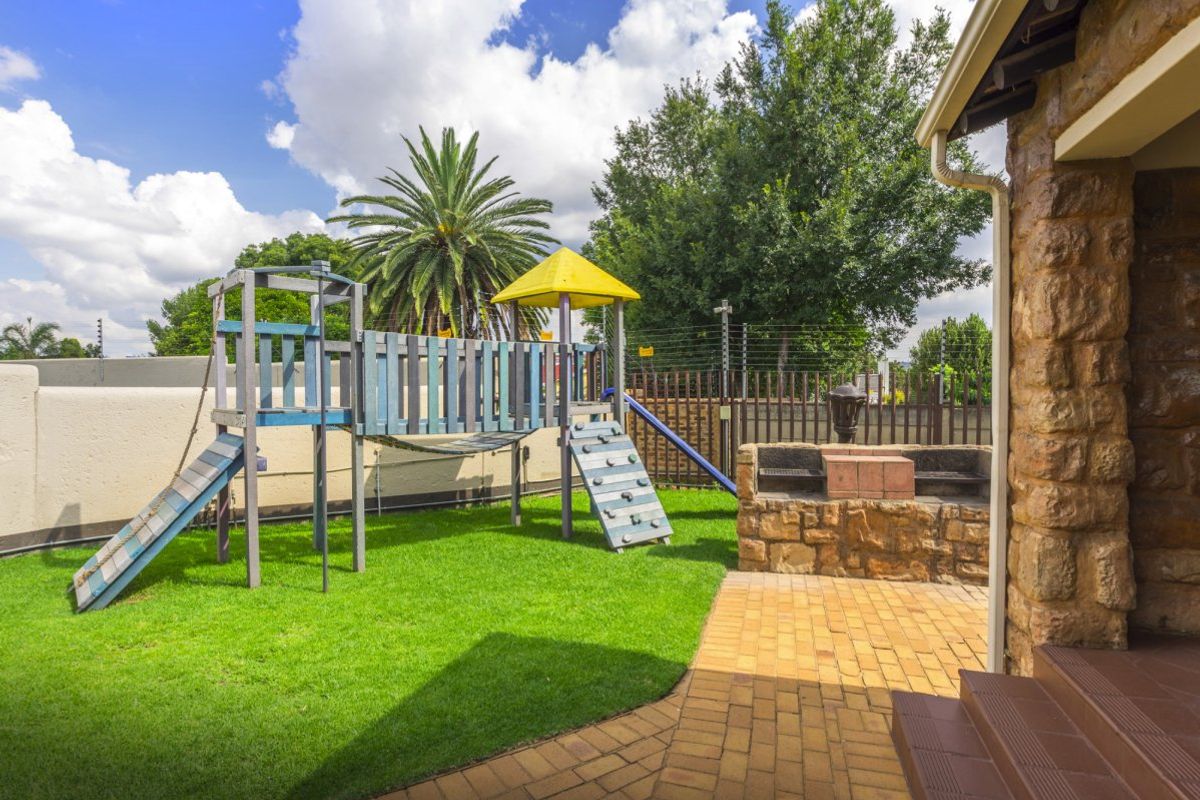 A private rear garden featuring a paved patio area with a built-in stone braai and a dedicated play area with lawn.