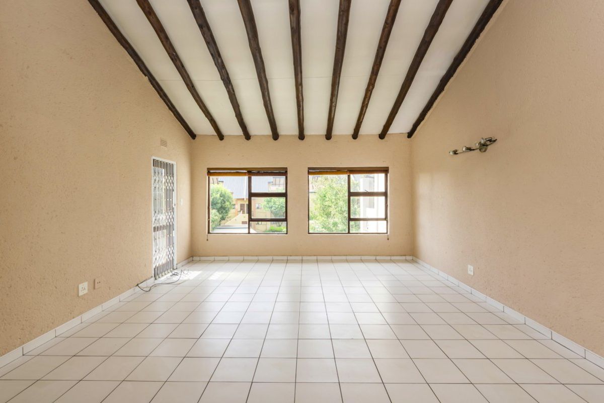 Spacious, empty living area featuring exposed timber ceiling beams, neutral tiled flooring, and large windows providing natural light.