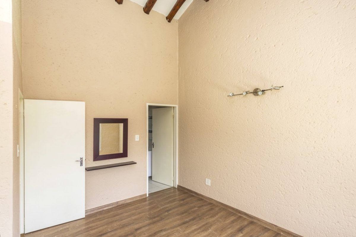 An empty bedroom featuring high ceilings with exposed timber beams, textured walls, and laminate flooring, offering a blank canvas for personalization.