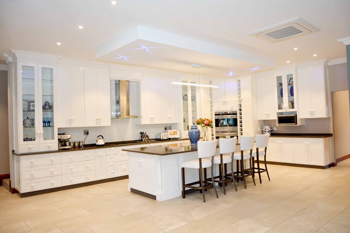 Spacious modern kitchen featuring white cabinetry, a large central island with seating, stone countertops, and integrated appliances under recessed lighting.