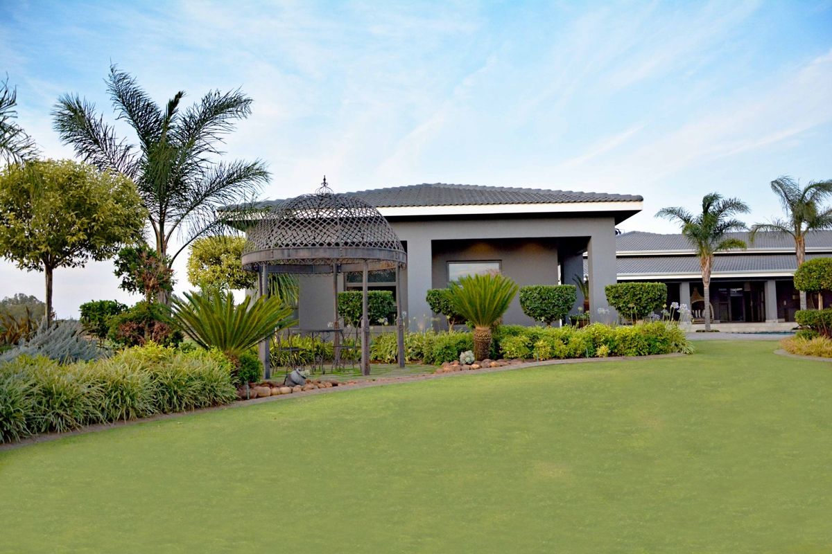 A well-maintained rear garden featuring a manicured lawn, established landscaping, and a covered patio area attached to the main residence.