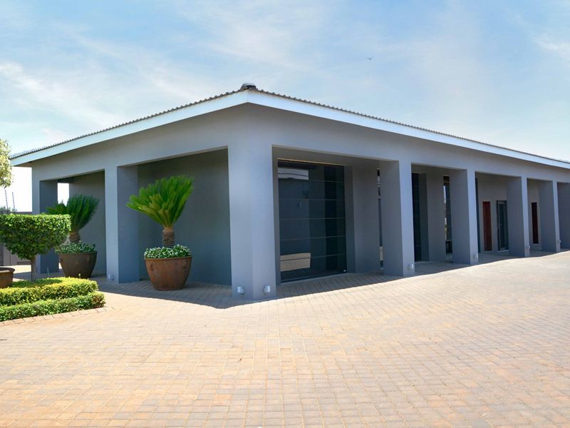 Modern exterior view of the property featuring a spacious covered patio area, concrete pillars, and a neatly paved driveway.