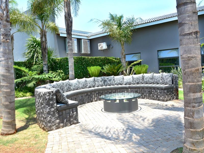 A well-maintained outdoor patio area featuring built-in stone seating, paved flooring, and established garden landscaping, set against the rear facade of the house.