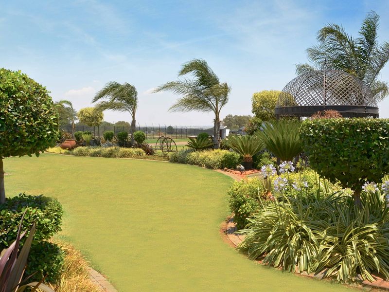 A well-maintained landscaped garden featuring a manicured lawn, mature ornamental shrubs, palm trees, and a decorative metal gazebo structure.