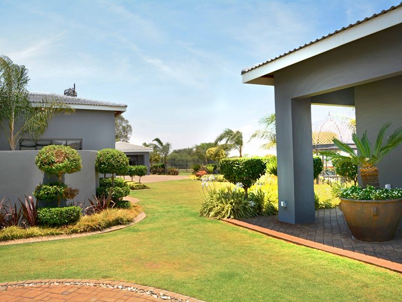 A well-maintained landscaped garden featuring a paved walkway, manicured lawn, and a covered patio area connecting the property structures.