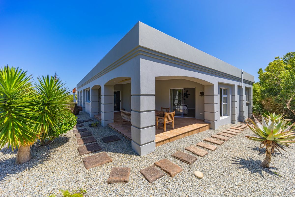 A well-maintained rear exterior view featuring a covered patio with tiled flooring, sliding glass doors, and a landscaped garden with stone pathways.