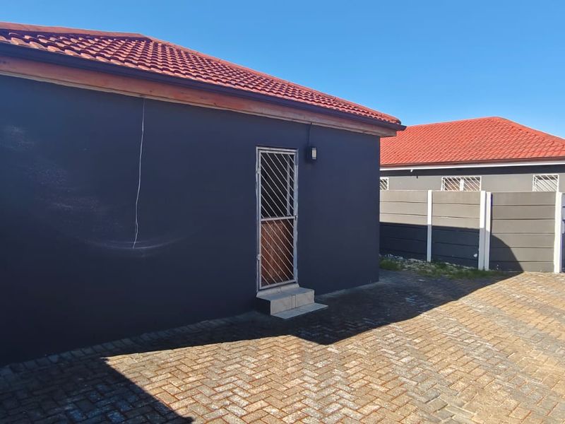 Rear exterior view of the property featuring a dark painted facade, tiled roof, paved driveway, and secure perimeter walling.