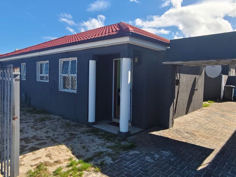 Front exterior view of a single-story house featuring a tiled roof, paved driveway with carport, and security fencing.