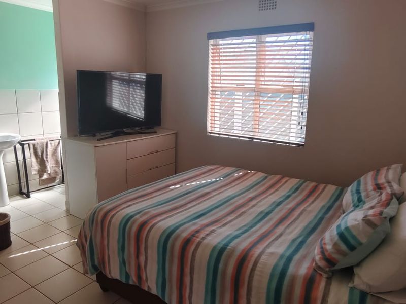 A bedroom featuring tiled flooring and an en-suite bathroom area with a pedestal basin, complemented by venetian blinds on the window.