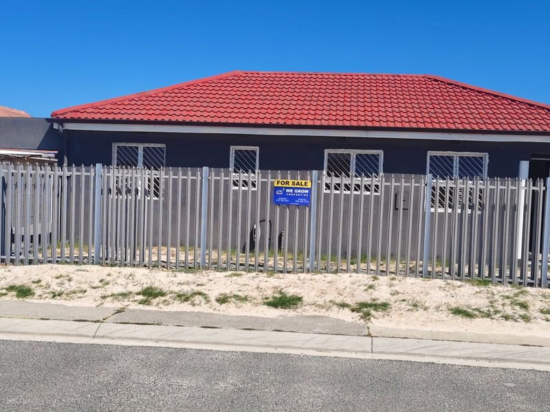 Front view of a single-story house featuring a red tiled roof, dark exterior walls, and secure metal perimeter fencing.