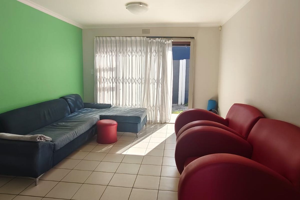 A living room featuring tiled flooring and a sliding glass door with a security gate, providing access to the exterior.