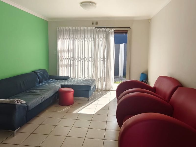 A living room featuring tiled flooring and a sliding glass door with a security gate, providing access to the exterior.