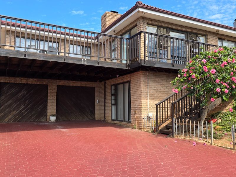 Front elevation of a double-story brick house featuring a paved driveway, double garage, and a large raised balcony with external staircase access.