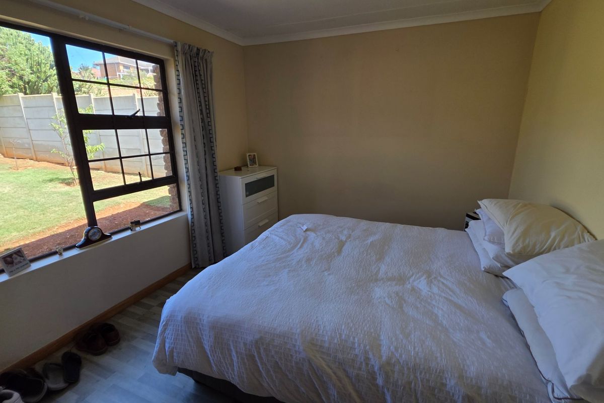 A bedroom featuring laminate flooring and a large window overlooking the garden area.