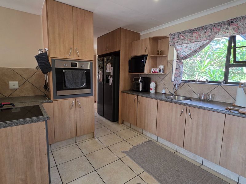 A functional kitchen featuring wood-look laminate cabinetry, tiled backsplash, built-in oven, and electric hob with ample counter space and natural light.