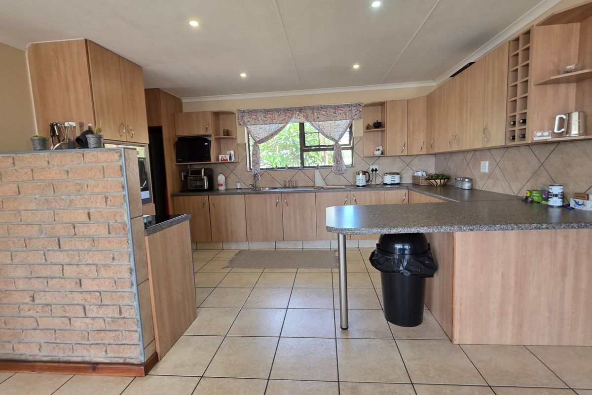 A functional kitchen featuring light wood-look cabinetry, tiled flooring, a brick feature wall, and a breakfast bar with ample counter space.