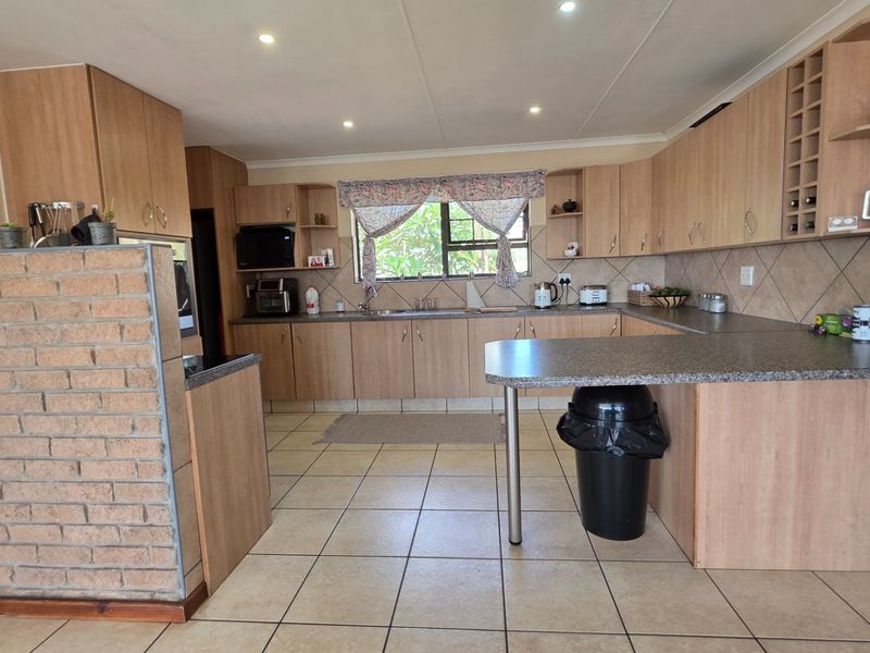 A functional kitchen featuring light wood-look cabinetry, tiled flooring, a brick feature wall, and a breakfast bar with ample counter space.
