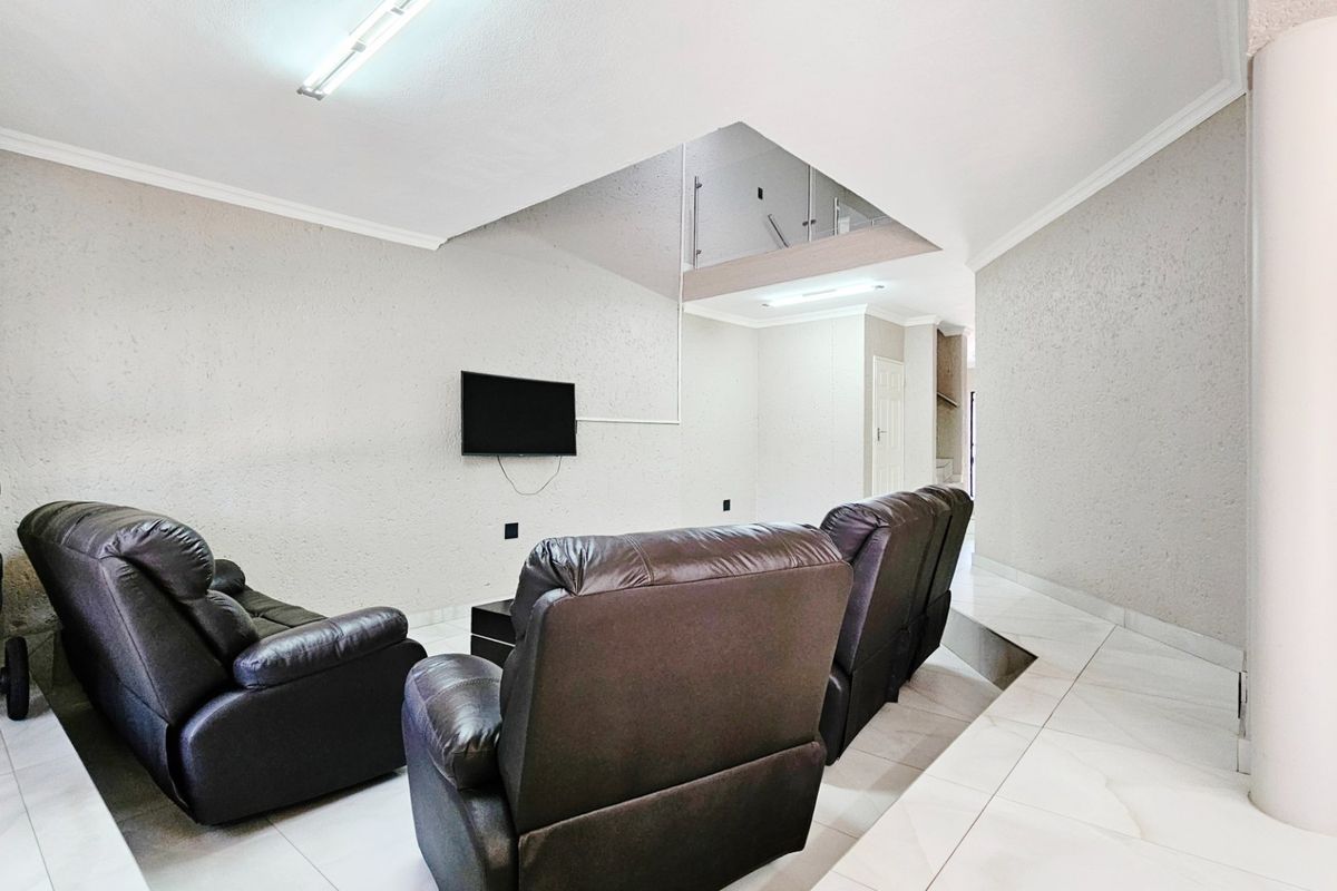 A spacious living area featuring tiled floors, a modern glass balustrade, and a structural column, offering an open-plan layout with neutral wall finishes.