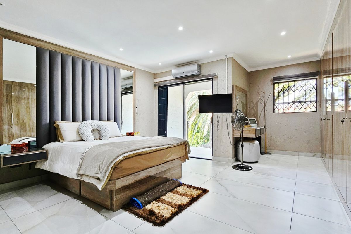 Spacious bedroom featuring modern tiled flooring, extensive built-in cupboards, an upholstered headboard, and direct access to an outdoor area via sliding glass doors.
