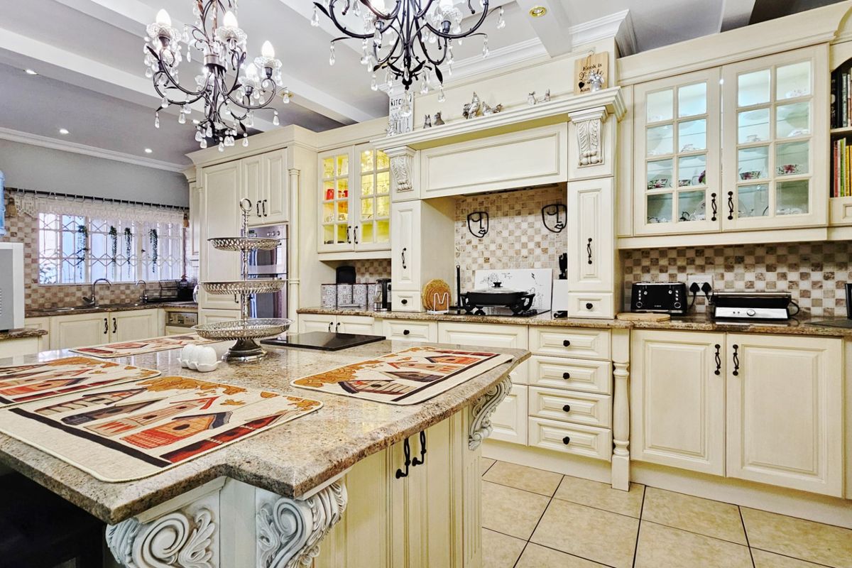 Spacious traditional kitchen featuring cream cabinetry, granite countertops, a large central island, and decorative chandeliers, offering a classic and functional culinary space.