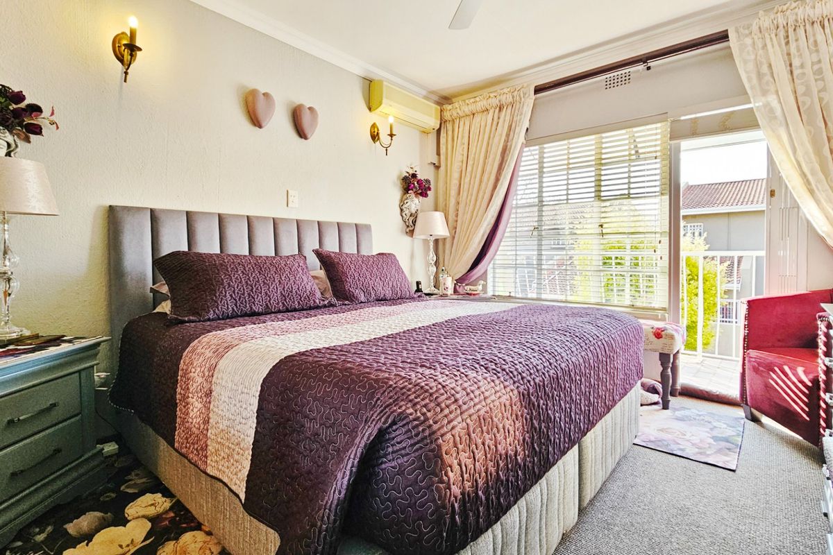A well-lit bedroom featuring a wall-mounted air conditioning unit, ceiling fan, and sliding glass door access to a private balcony.